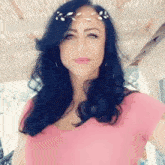 a woman wearing a pink shirt and a flower crown on her head is looking at the camera .