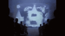 a group of people are standing in front of a large screen .