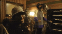 a man wearing a bucket hat and sunglasses is standing in front of a microphone in a recording studio .