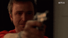 a man in a red shirt is pointing a gun at the camera with a netflix logo in the background