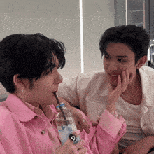 a man in a pink shirt is drinking from a bottle with a straw that says ' aquafina ' on it