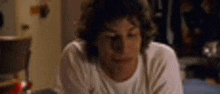 a man in a white shirt is laying on a bed looking down .