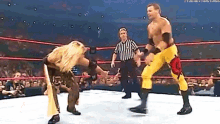 two wrestlers are fighting in a wrestling ring with a referee watching .