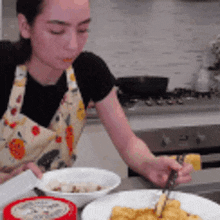 a woman in an apron is sitting at a table eating food with a fork .