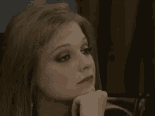 a close up of a woman 's face with her eyes closed and her hand on her chin