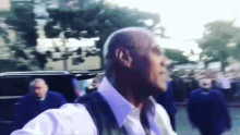 a bald man in a white shirt and vest walks down a street