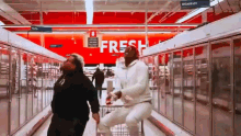 two people are dancing in a grocery store with a sign that says fresh .