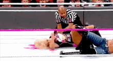 a woman is laying on the ground in a wrestling ring while a referee stands behind her .