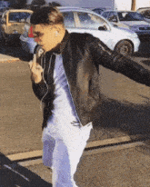 a man wearing ear buds and a black jacket is standing in a parking lot with his arms outstretched