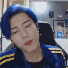 a man with blue hair is wearing a blue and yellow jacket and sitting in a chair .