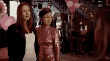 two women are standing next to each other in a room with pink balloons and hearts .