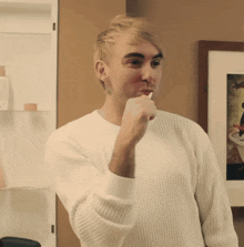 a man in a white sweater is brushing his teeth in front of a picture