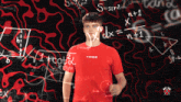 a man wearing a red tribe shirt stands in front of a wall of mathematical equations
