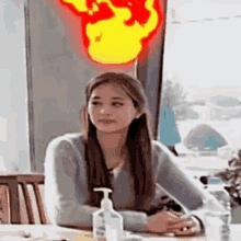a woman is sitting at a table with a bottle of hand sanitizer and a bottle of water .