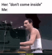 a man is playing a piano and singing into a microphone while wearing a white tank top .