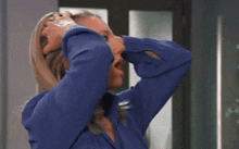 a woman in a blue shirt is holding her head with her hands