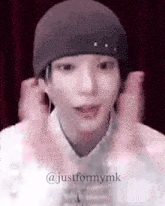 a close up of a person wearing a beanie and making a heart shape with their hands .