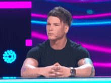 a man in a black shirt is sitting with his hands folded in front of a purple background