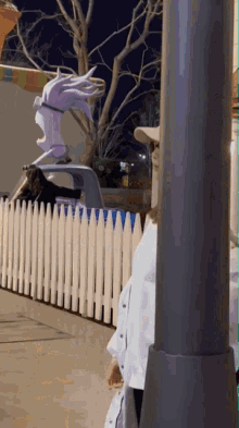 a woman stands in front of a white picket fence and a statue