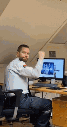 a man sitting at a desk with his fist in the air in front of a computer monitor