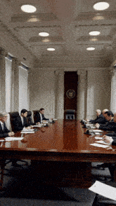 a group of men are sitting around a long wooden table in a conference room