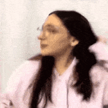 a woman with pigtails and glasses is wearing a pink hoodie and a white shirt .