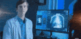 a man in a white coat is standing in front of a computer monitor .