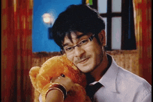 a man wearing glasses holds a teddy bear in his arms