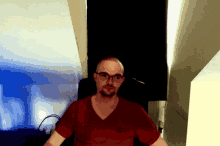 a man wearing glasses and a red shirt stands in a dark room