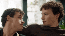 two young men with curly hair are touching noses