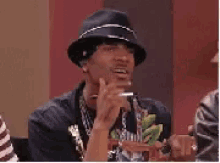 a man wearing a hat and a necklace is smoking a cigarette