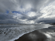 a cloudy sky over the ocean with waves crashing on the beach