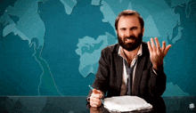 a man with a beard is sitting at a desk in front of a map