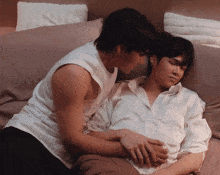 two men are laying on a bed with one wearing a white shirt with the letter s on the pocket