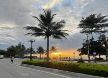 a group of people are walking along a sidewalk near the beach at sunset