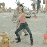 a woman in a pink bikini stands on a sidewalk next to a man in a statue of liberty outfit