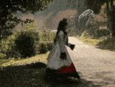 a woman in a white and red dress is walking down a dirt road