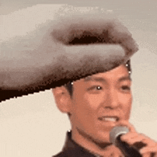 a man is holding a microphone in front of his face and a hand is holding a hat on his head .