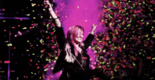 a woman is standing on a stage with her arms in the air while confetti is falling around her .