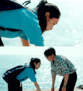 a man and a woman are looking at each other in front of the ocean