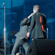a man in a suit stands next to another man in a black suit
