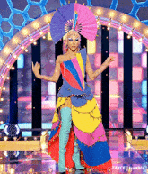 a woman in a colorful costume with a fan on her head is on a stage