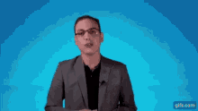 a man in a suit and glasses is talking on a blue background .