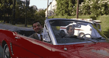 a man in a suit and tie is driving a red convertible car with another man sitting in the back seat .