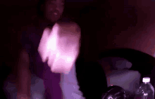 a man in a purple shirt is dancing in a dark room with a bottle of water in the background .