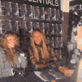 two women are sitting in front of a wall with essentials written on it