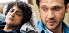 a man with curly hair laying on a couch next to another man with a beard