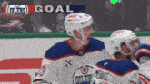 two hockey players are celebrating a goal in front of a scoreboard