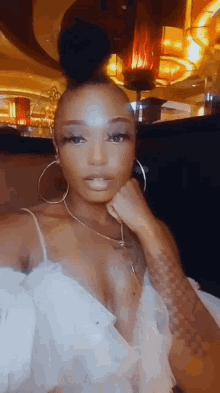 a woman in a white dress is taking a selfie with her hand on her chin