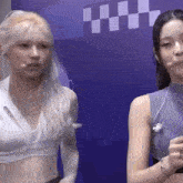 two women are standing next to each other in front of a blue wall with a checkered pattern on it .